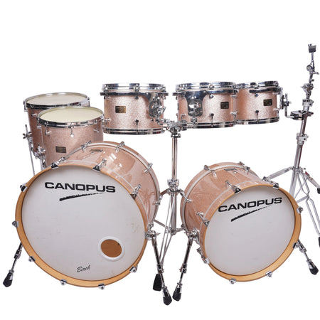 A Canopus drum kit with a glittery rose gold finish, chrome hardware, and white drum heads, photographed against a plain white studio background.