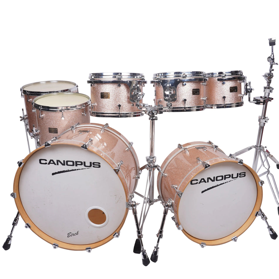 A Canopus drum kit with a glittery rose gold finish, chrome hardware, and white drum heads, photographed against a plain white studio background.